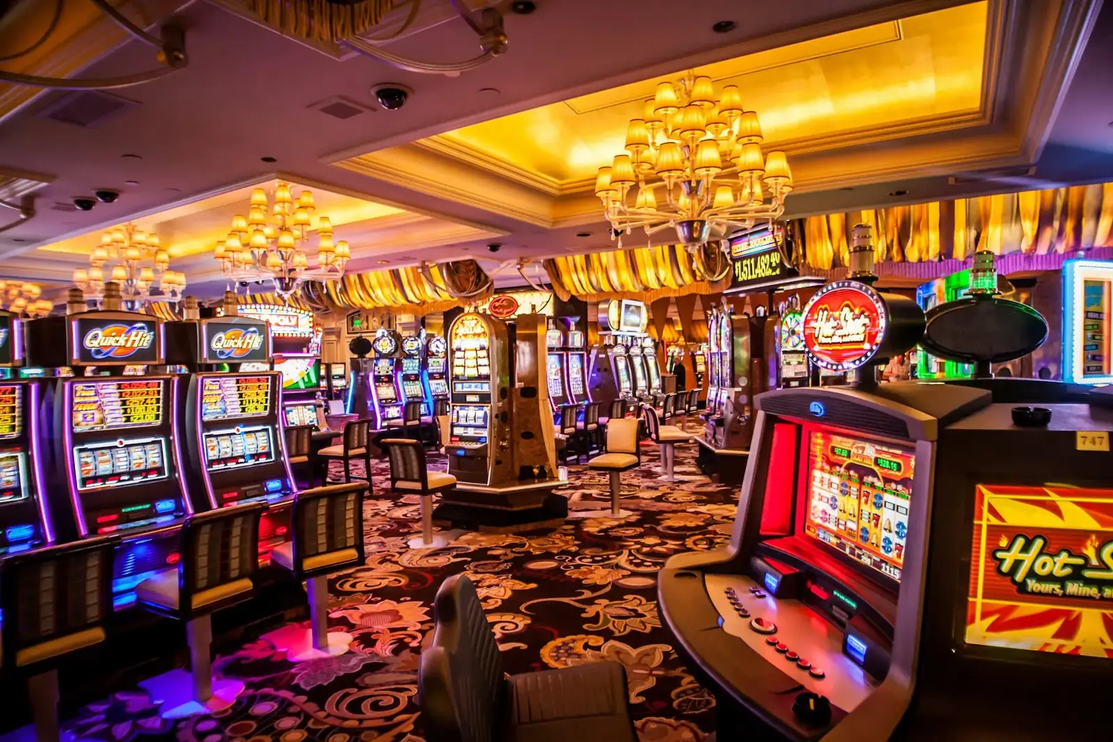 A brightly lit casino floor with rows of slot machines under chandeliers