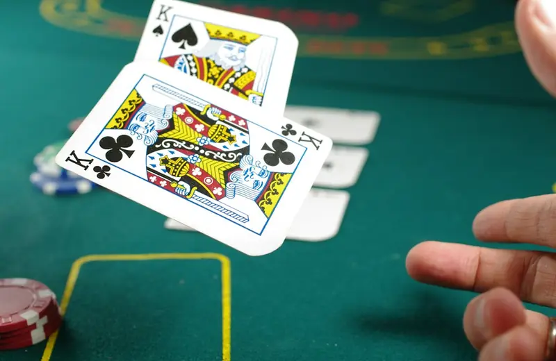 Playing cards in mid-air over a green table while a hand reaches in